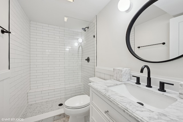 bathroom featuring a tile shower, vanity, and toilet