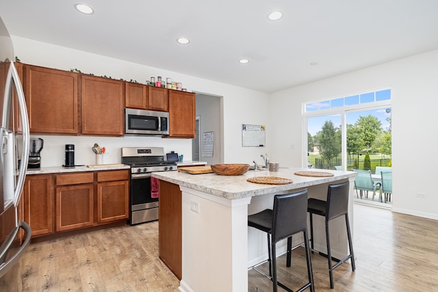 kitchen featuring a kitchen breakfast bar, stainless steel appliances, a kitchen island with sink, and light hardwood / wood-style floors