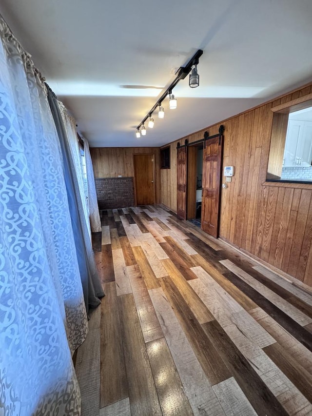 hallway featuring hardwood / wood-style floors, a barn door, rail lighting, and wooden walls