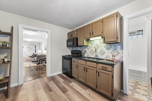 kitchen with sink, light wood-type flooring, backsplash, and black appliances