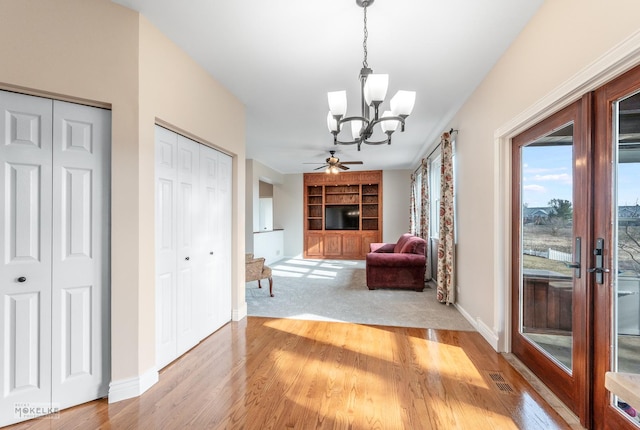 corridor featuring french doors, built in features, an inviting chandelier, and light hardwood / wood-style flooring