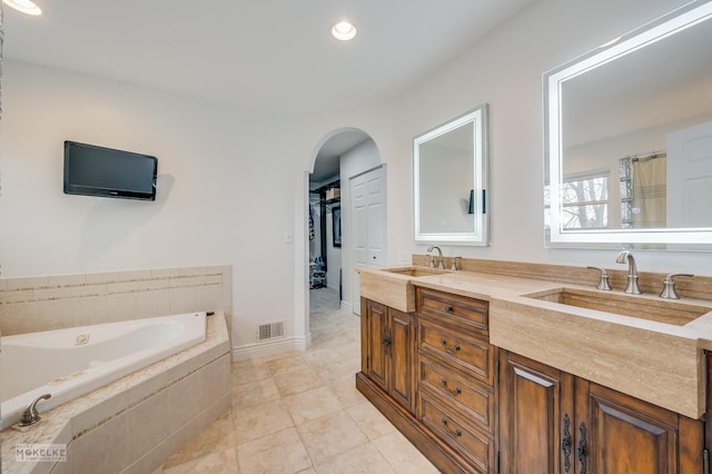 bathroom with tile patterned flooring, vanity, and tiled bath