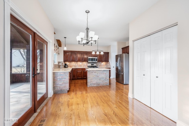 kitchen with pendant lighting, appliances with stainless steel finishes, backsplash, a notable chandelier, and light wood-type flooring