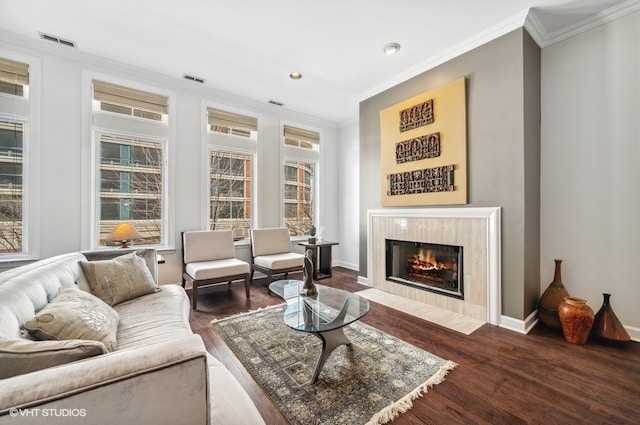 living room featuring a tiled fireplace, dark hardwood / wood-style floors, and ornamental molding