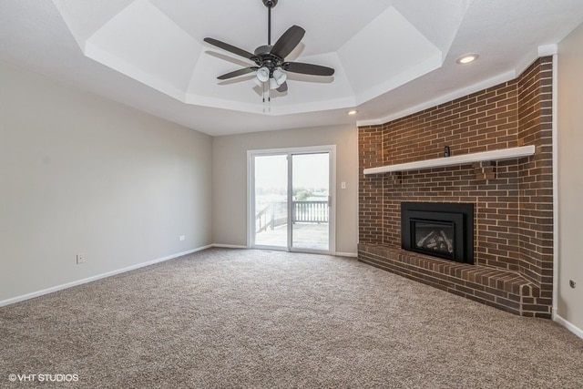 unfurnished living room featuring a fireplace, carpet floors, a tray ceiling, and ceiling fan