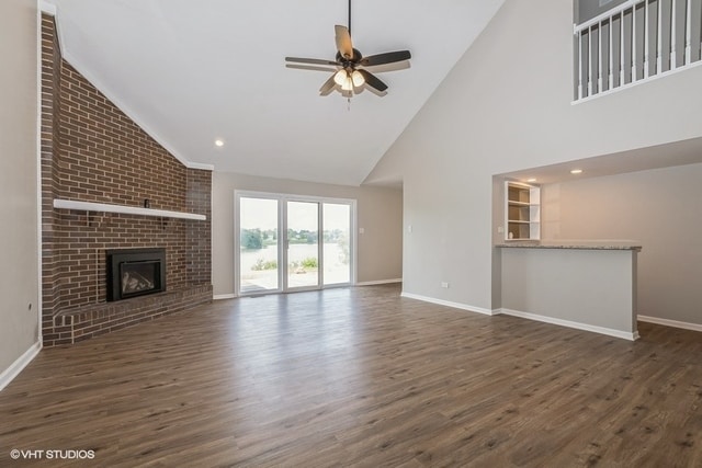 unfurnished living room featuring ceiling fan, high vaulted ceiling, dark hardwood / wood-style floors, and a brick fireplace