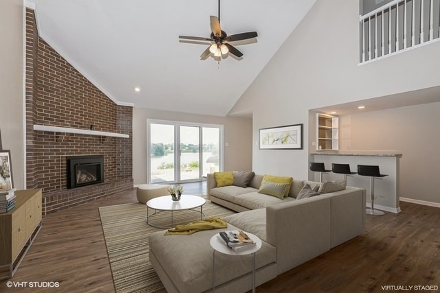 living room with ceiling fan, dark hardwood / wood-style flooring, high vaulted ceiling, and a brick fireplace