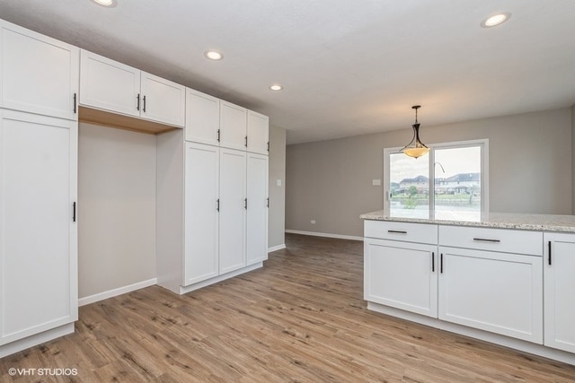 kitchen with white cabinets, decorative light fixtures, light hardwood / wood-style flooring, and light stone countertops