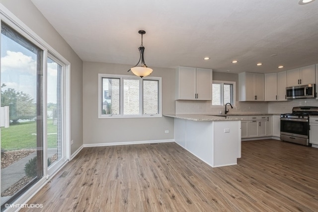 kitchen featuring white cabinetry, kitchen peninsula, appliances with stainless steel finishes, and light hardwood / wood-style flooring