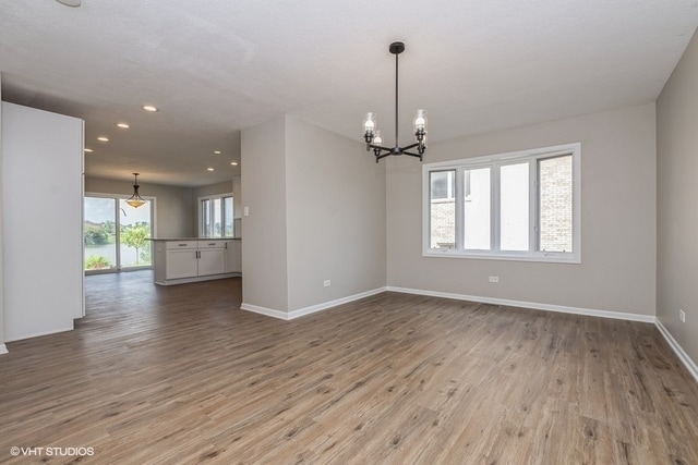 empty room with hardwood / wood-style floors, plenty of natural light, and an inviting chandelier