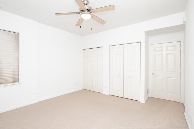 unfurnished bedroom with ceiling fan, light colored carpet, and two closets