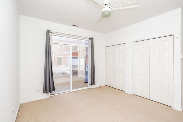 unfurnished bedroom featuring ceiling fan, light carpet, and multiple closets