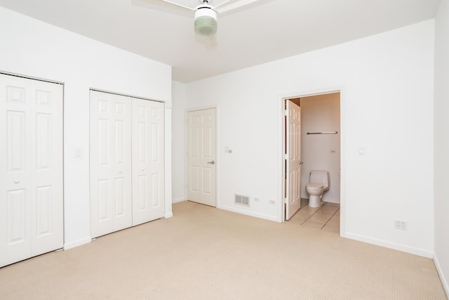 unfurnished bedroom featuring ensuite bath, ceiling fan, light carpet, and multiple closets