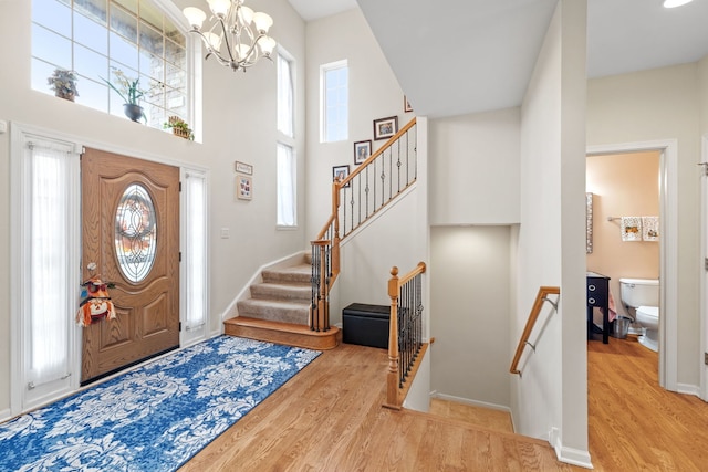 foyer entrance featuring a notable chandelier, a healthy amount of sunlight, a towering ceiling, and light hardwood / wood-style flooring