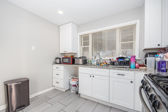 kitchen with light stone countertops, white cabinets, sink, and stainless steel range