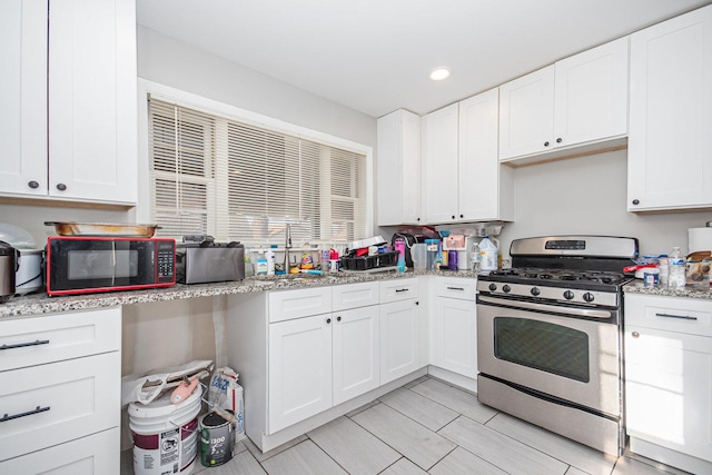 kitchen with light stone counters, white cabinetry, and gas stove