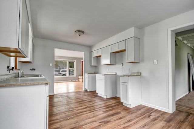 kitchen with white cabinetry, baseboards, a sink, and wood finished floors