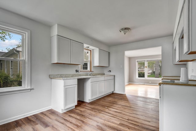 kitchen featuring baseboards, light countertops, light wood-style flooring, and a sink
