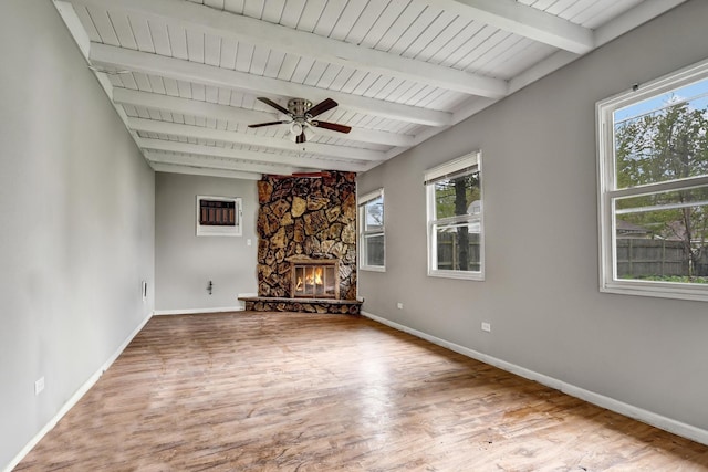 unfurnished living room with ceiling fan, beam ceiling, a fireplace, baseboards, and wood finished floors
