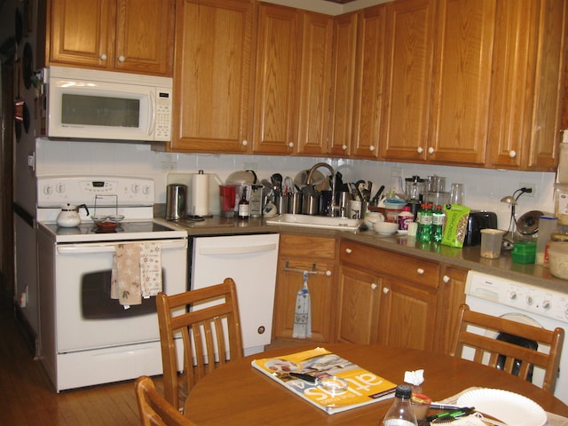 kitchen featuring decorative backsplash, white appliances, dark wood-type flooring, sink, and washer / dryer