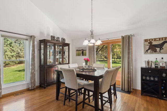 dining area featuring hardwood / wood-style flooring, a notable chandelier, and high vaulted ceiling