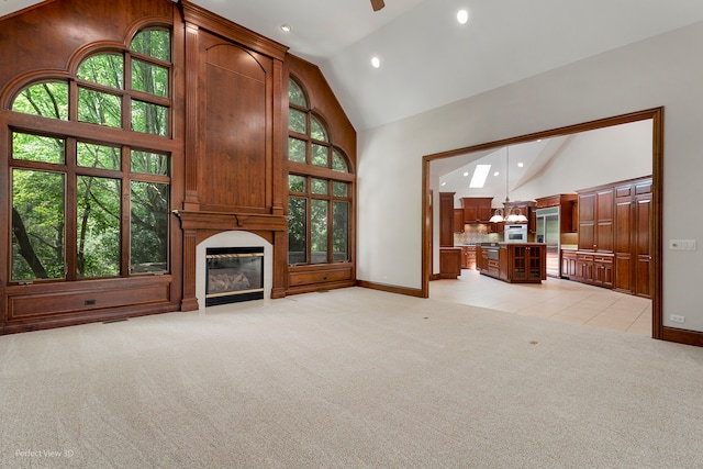 unfurnished living room with a large fireplace, light colored carpet, high vaulted ceiling, and ceiling fan