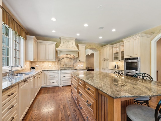 kitchen featuring premium range hood, a kitchen bar, arched walkways, and a sink