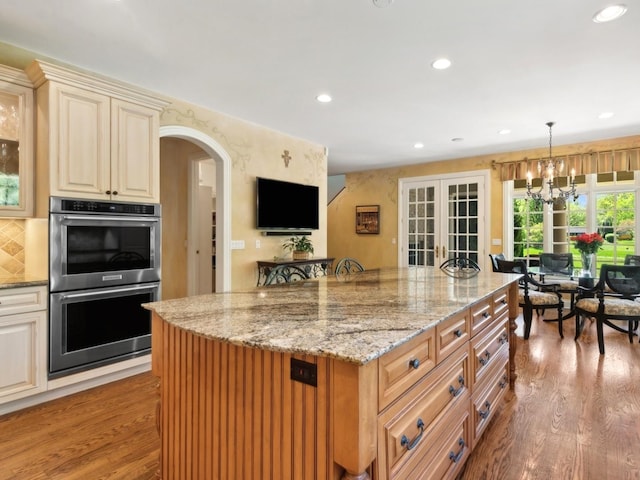 kitchen with stainless steel double oven, cream cabinetry, arched walkways, and wood finished floors