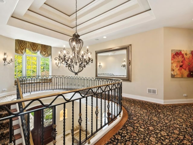 corridor with a notable chandelier, visible vents, baseboards, a tray ceiling, and crown molding