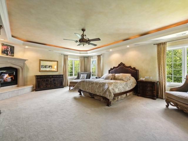 bedroom featuring ornamental molding, a glass covered fireplace, a raised ceiling, and carpet flooring