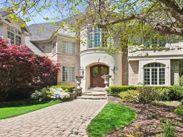 property entrance with brick siding, stucco siding, and french doors