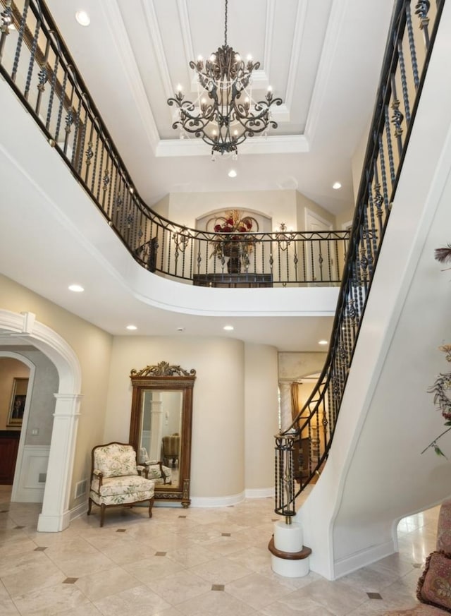 foyer featuring a tray ceiling, stairs, arched walkways, and crown molding