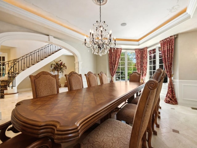 dining space with a tray ceiling, arched walkways, a decorative wall, ornamental molding, and wainscoting