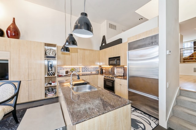 kitchen featuring high end refrigerator, dark stone counters, sink, range, and hanging light fixtures