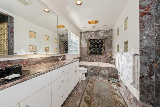 bathroom featuring vanity, toilet, tile walls, and tiled bath