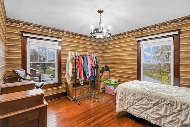 bedroom featuring log walls, wood-type flooring, and an inviting chandelier