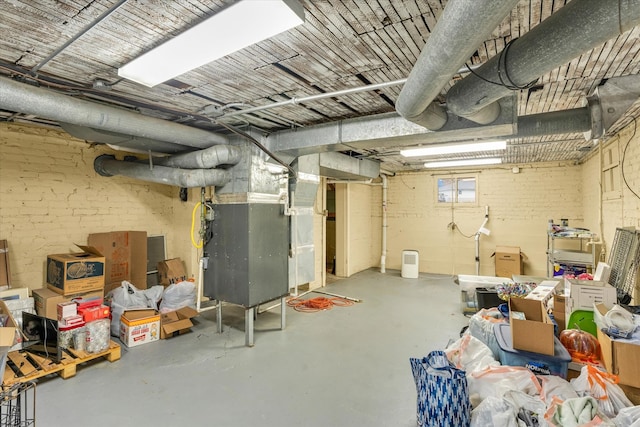 basement featuring brick wall and heating unit