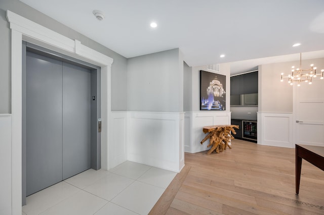 hall featuring elevator, light hardwood / wood-style flooring, beverage cooler, and a notable chandelier