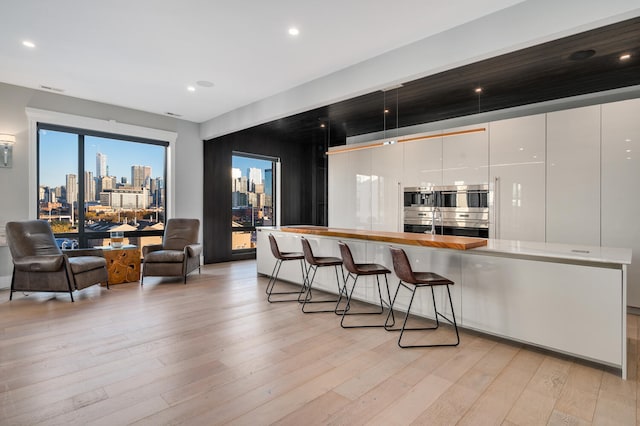 kitchen with white cabinets, a breakfast bar, double oven, and light hardwood / wood-style flooring