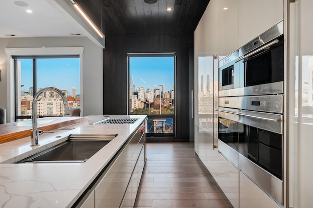 kitchen featuring white cabinetry, sink, stainless steel double oven, light stone counters, and dark hardwood / wood-style flooring