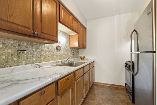 kitchen with light stone countertops, tasteful backsplash, black range with gas cooktop, sink, and stainless steel refrigerator