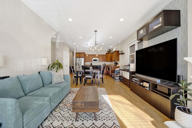 living room with light hardwood / wood-style floors, ornamental molding, and a notable chandelier