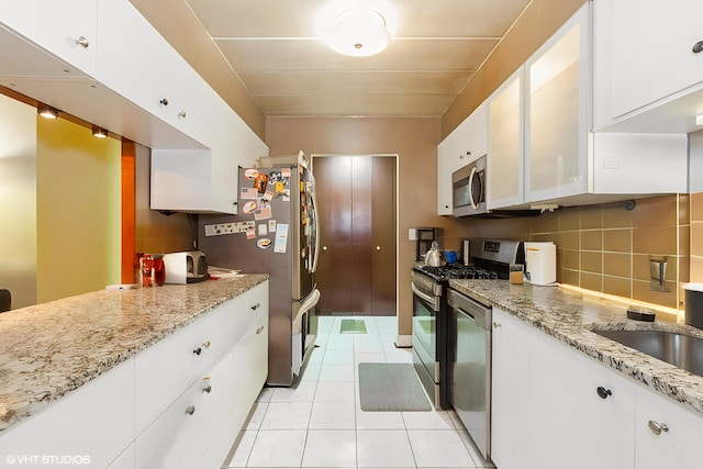 kitchen with light tile patterned floors, appliances with stainless steel finishes, white cabinetry, and decorative backsplash