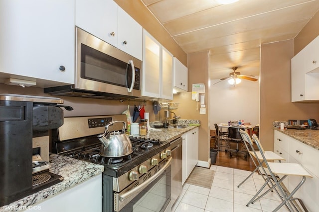 kitchen with ceiling fan, light stone counters, light tile patterned flooring, stainless steel appliances, and white cabinetry