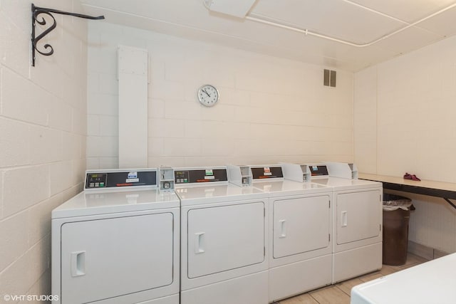 community laundry room with concrete block wall, washing machine and dryer, and visible vents