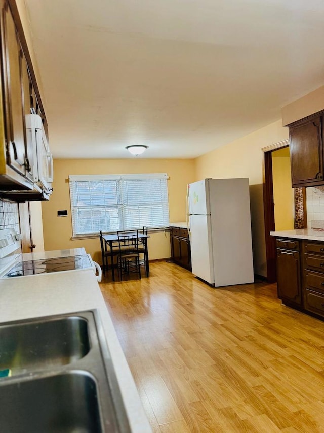 kitchen with light wood-type flooring, white appliances, dark brown cabinetry, and tasteful backsplash