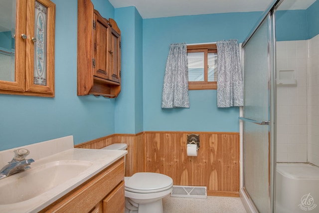 bathroom with vanity, toilet, a shower with door, and wooden walls