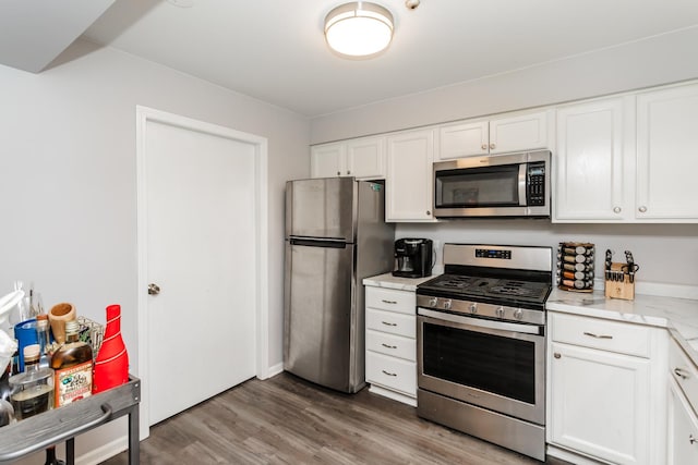 kitchen with white cabinetry, stainless steel appliances, light stone counters, and wood-type flooring