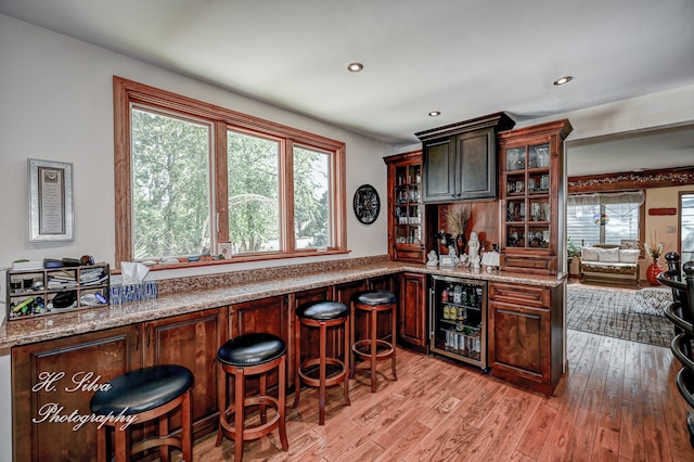 bar featuring light hardwood / wood-style floors, light stone counters, and wine cooler