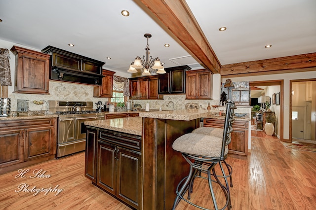 kitchen with light stone countertops, stainless steel gas range oven, beamed ceiling, a kitchen island, and light wood-type flooring